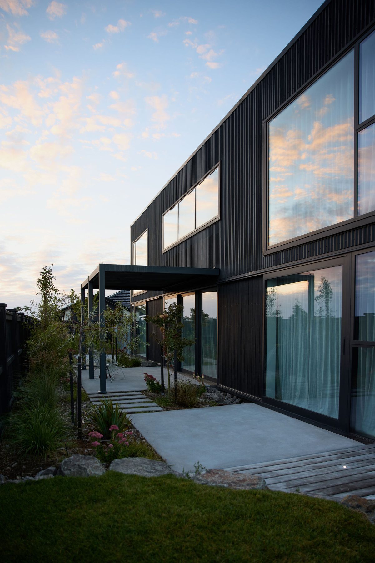 The garden edge at dusk, living spaces glowing behind glass.