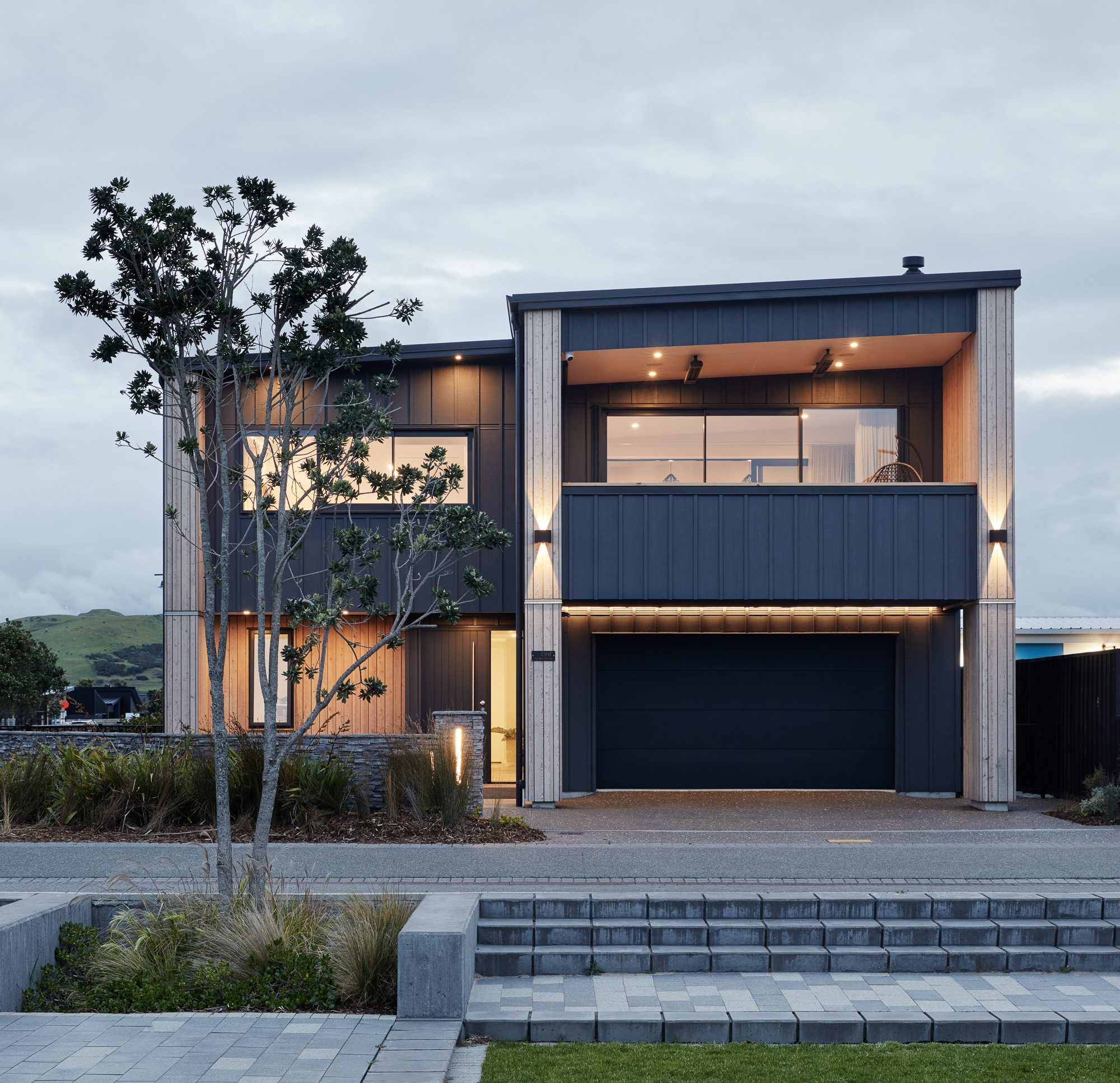 Otira Close House: the courtyard at dusk, both storeys glowing.